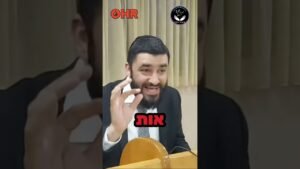 Bearded man in a suit speaking at a podium, gesturing with his right hand; red Hebrew text overlay and two logos in the top corners.