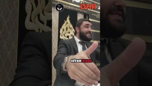 Bearded man in a suit extending his hand toward the camera in an ornate room; OHR logo and Hebrew caption overlay.