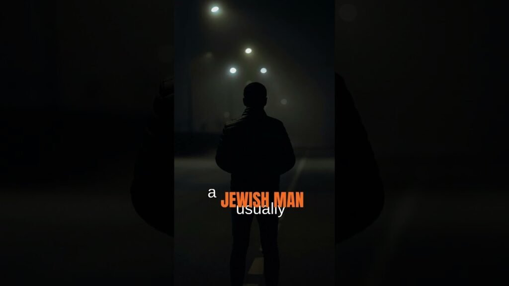 Back view of a man in a dark coat standing on a dimly lit night street, with bold orange text reading 'JEWISH MAN' overlaid across the center.
