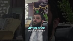 Bearded man in a suit sits in a synagogue, with ornate Torah ark and banners in the background; video subtitle text overlays the scene.