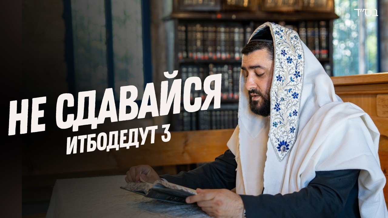 Man in a white prayer robe with blue embroidery reads a book at a table in a library.
