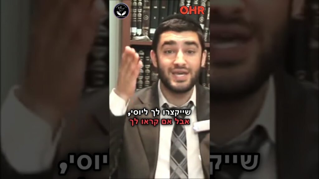 Bearded man in a suit speaking in front of a bookshelf, Hebrew subtitles on screen, OHR logo and another emblem in corners.”,