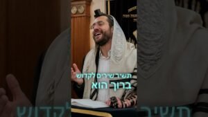 Rabbi or Jewish man in a tallit singing or speaking at a synagogue, with tefillin on his arm and head.