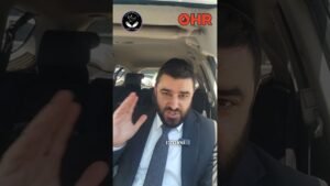 Man in a suit inside a car, speaking and gesturing with a raised hand; Hebrew subtitle 'שאנחנו' visible with logos above.