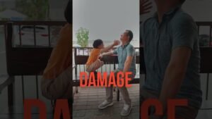 Boy in orange shirt reaches toward a man seated on a bench outdoors; bold red text 'DAMAGE' overlays the scene, suggesting a dramatic moment.