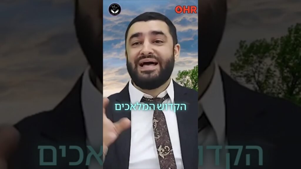 Bearded man in a suit and tie speaking to the camera outdoors, with a blue sky and trees behind, turquoise Hebrew subtitle overlay visible.